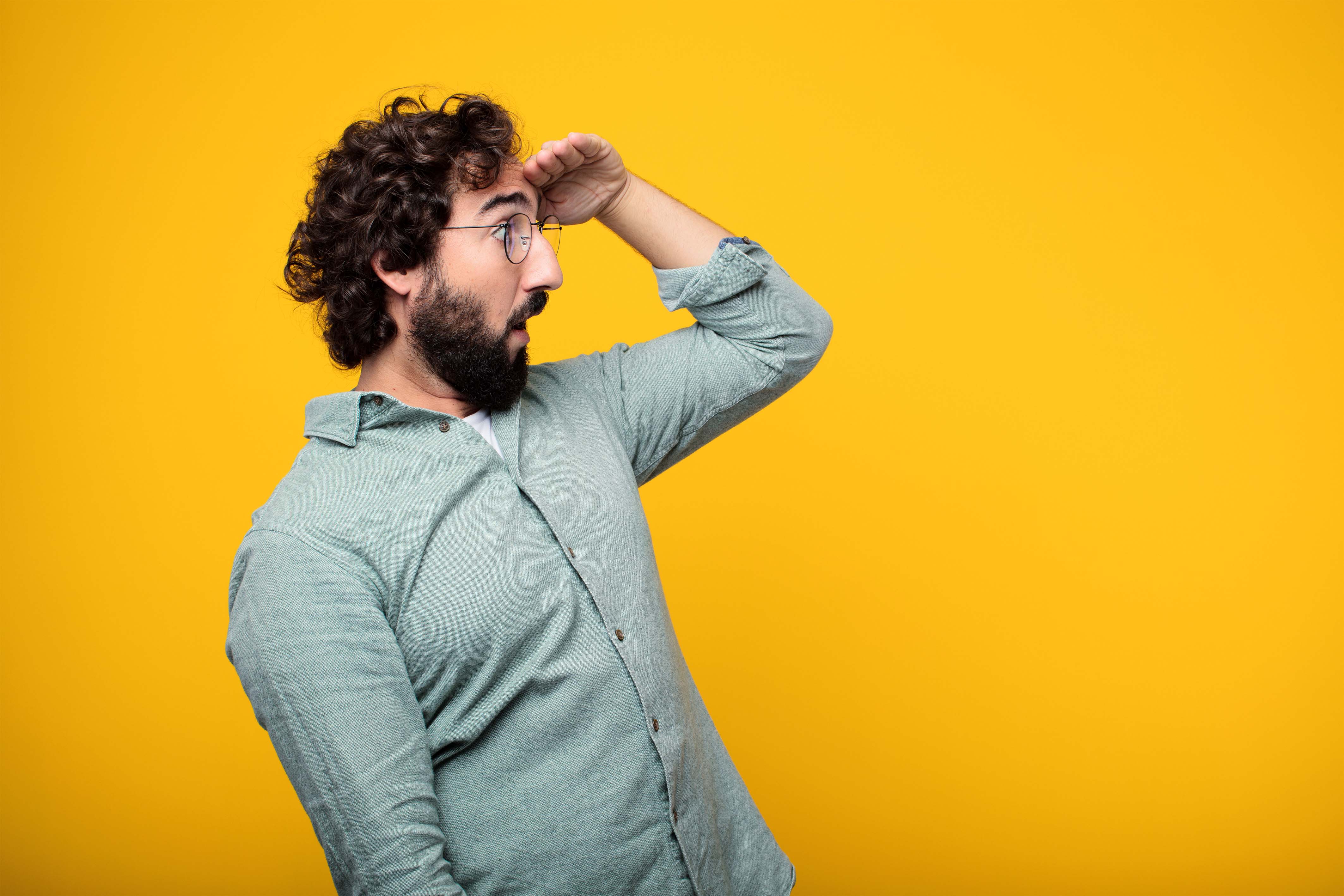 Hombre inclinado hacia su izquierda mirando el horizonte en fondo amarillo